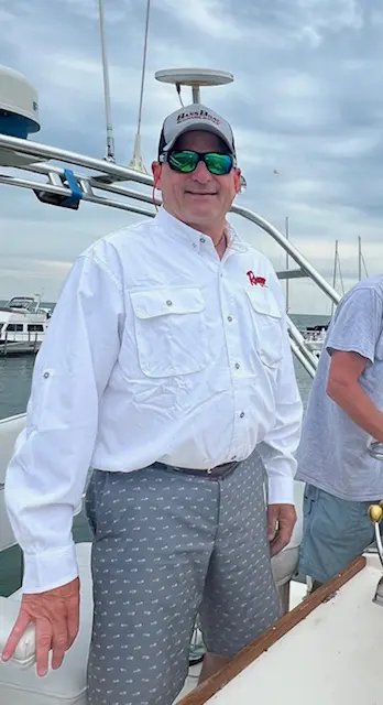 A man in white shirt and sunglasses standing on boat.